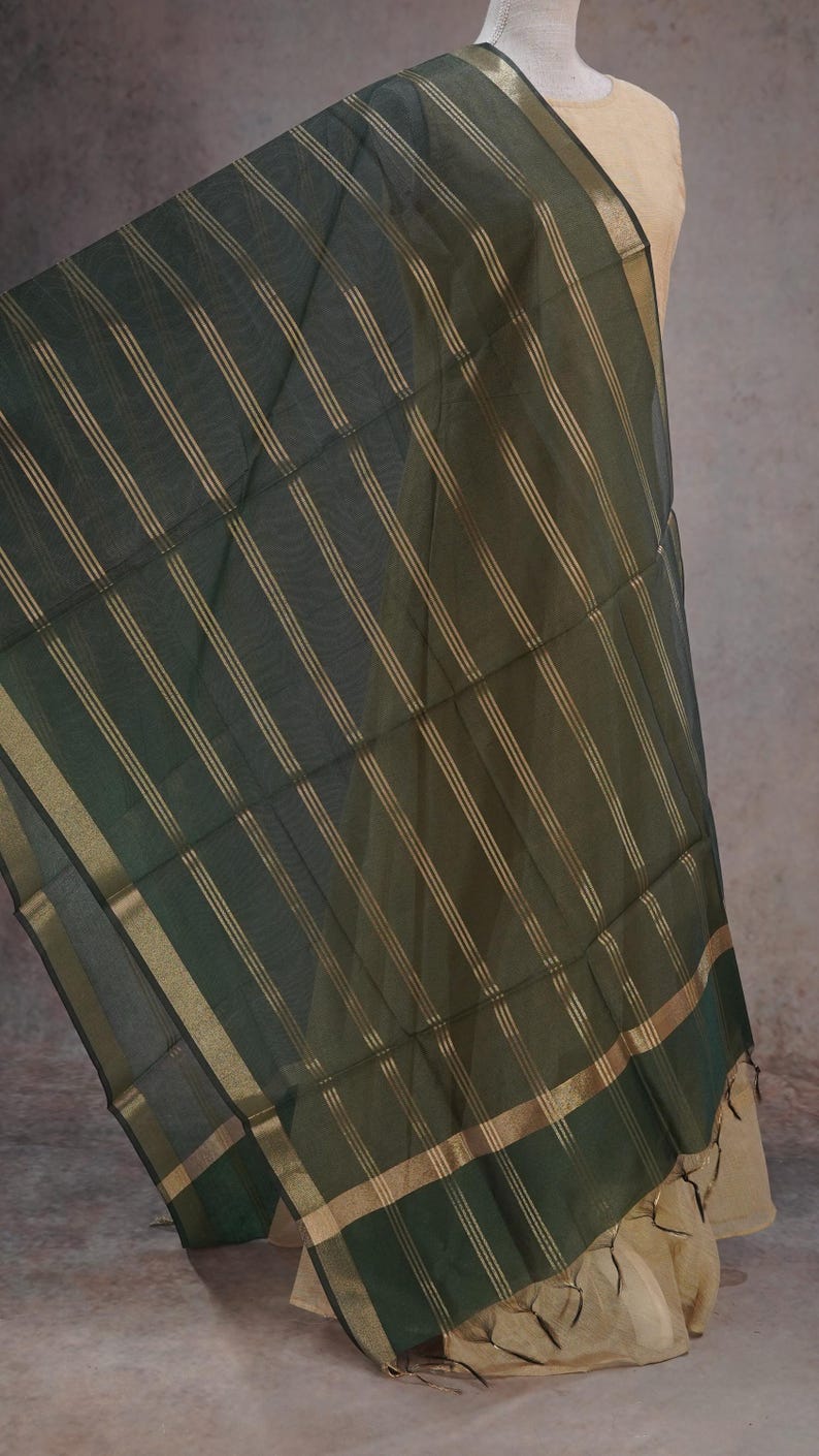 May include: Dark green sheer fabric with gold vertical stripes and gold trim. The fabric is draped over a mannequin, showcasing its flowing texture and design. The fabric has a subtle sheen.