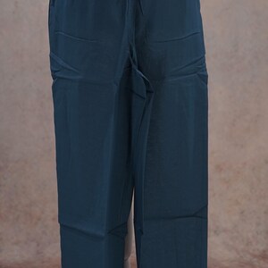 May include: Dark teal-colored pants with a relaxed fit. The pants have a drawstring waistband and pockets. The fabric has a slight sheen. The pants are displayed on a mannequin.