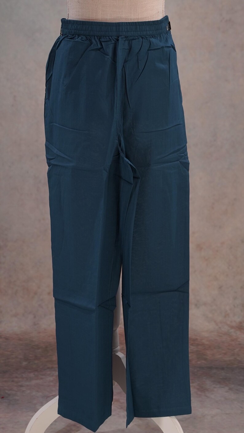 May include: Dark teal-colored pants with a relaxed fit. The pants have a drawstring waistband and pockets. The fabric has a slight sheen. The pants are displayed on a mannequin.