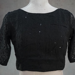 Peut inclure: Haut noir à manches courtes et col bateau. Le haut est fait d'un tissu en dentelle délicat et à motifs. De petits sequins brillants sont parsemés sur le devant. Les manches sont de longueur coude.