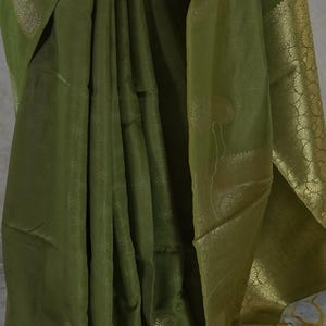Puede incluir: Sari verde oliva con detalles dorados. La tela est&aacute; drapeada, mostrando patrones intrincados y un borde decorativo. El sari presenta dise&ntilde;os de cachemira y florales.