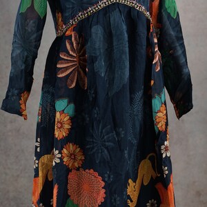 May include: A long, dark blue dress with a V-neck and long sleeves. The dress features a floral and animal print in orange, green, and yellow. The neckline and empire waist are embellished with colorful beads.