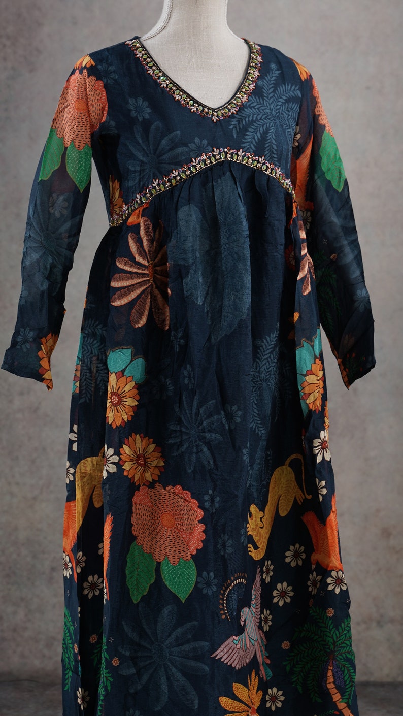 May include: A long, dark blue dress with a V-neck and long sleeves. The dress features a floral and animal print in orange, green, and yellow. The neckline and empire waist are embellished with colorful beads.