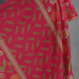 Puede incluir: Prenda rosa vibrante con estampado floral, con detalles de hojas verdes y flores naranjas. La tela presenta un patr&oacute;n repetido de hojas y flores, con un borde decorativo. La prenda se exhibe en un maniqu&iacute;.