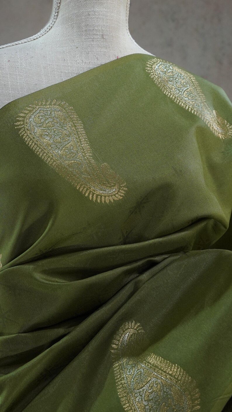 Puede incluir: Tela verde oliva con estampado de cachemir dorado. La tela est&aacute; drapeada, mostrando pliegues y sombras. El dise&ntilde;o de cachemir es detallado y se repite en la superficie, creando un textil lujoso.
