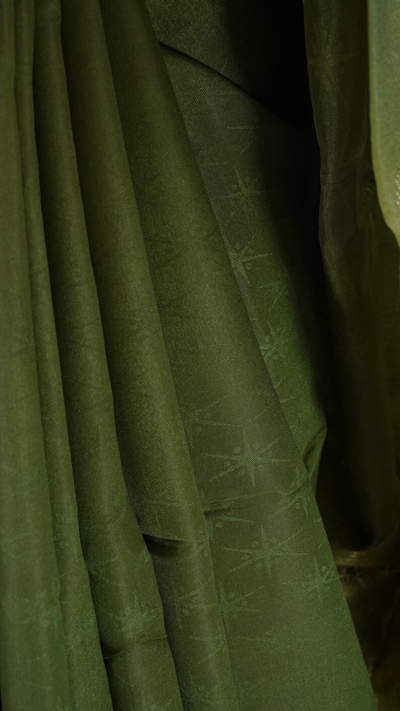 Puede incluir: Primer plano de tela verde oliva con sutiles patrones de estrellas. La tela est&aacute; drapeada en pliegues suaves, creando sombras y reflejos. La textura parece suave y ligeramente brillante, sugiriendo un material lujoso.