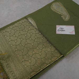 Puede incluir: Tela verde oliva con un dise&ntilde;o de cachemira dorada y un borde dorado estampado. La tela tiene una etiqueta que dice "Chic Boutique". La tela est&aacute; doblada y tiene flecos.