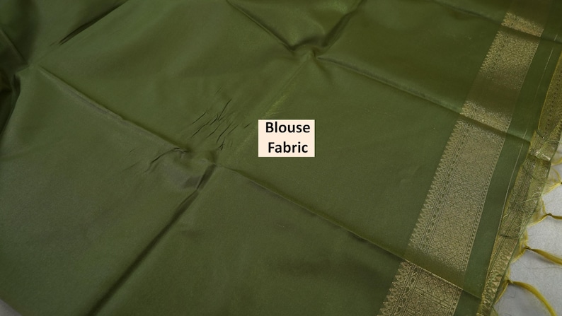 Puede incluir: Tela de blusa verde oliva con un borde dorado y el texto "Blouse Fabric". La tela est&aacute; doblada, mostrando una superficie texturizada. El borde tiene un dise&ntilde;o detallado con detalles dorados.