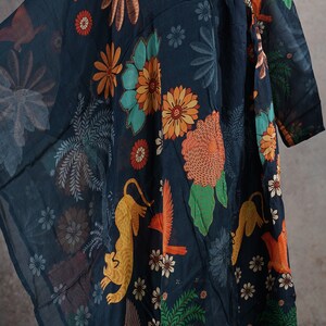 May include: Dark navy tunic with a vibrant floral and animal print. The design features orange birds, yellow leopards, and colorful flowers. The neckline is embellished with decorative stitching. The tunic is made of a lightweight, flowing fabric.