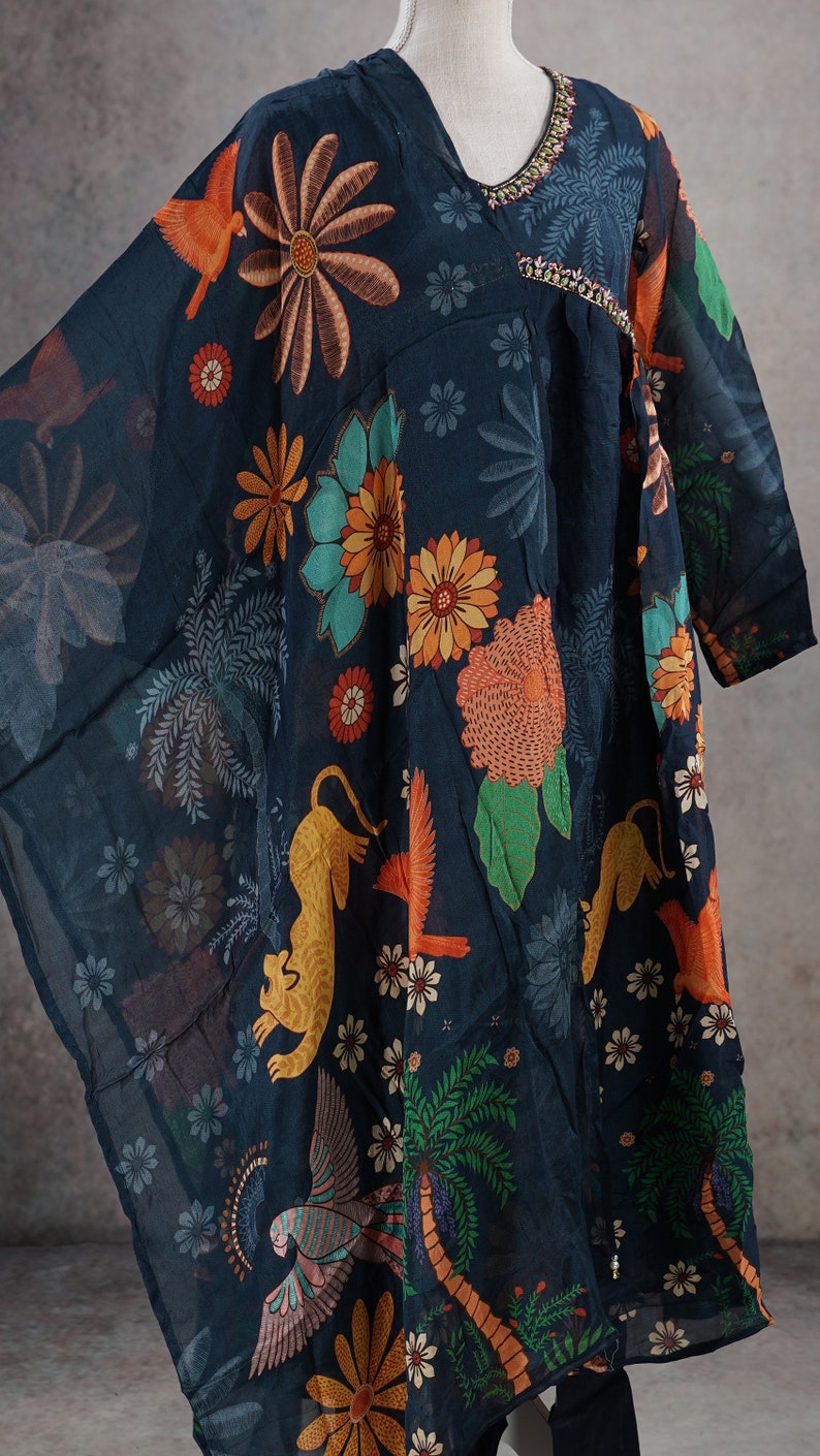 May include: Dark navy tunic with a vibrant floral and animal print. The design features orange birds, yellow leopards, and colorful flowers. The neckline is embellished with decorative stitching. The tunic is made of a lightweight, flowing fabric.