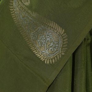 Puede incluir: Tela verde oliva con un detallado dise&ntilde;o de cachemira en oro y plata. La tela est&aacute; doblada, mostrando el intrincado dise&ntilde;o y la textura. La est&eacute;tica general es elegante y sofisticada.