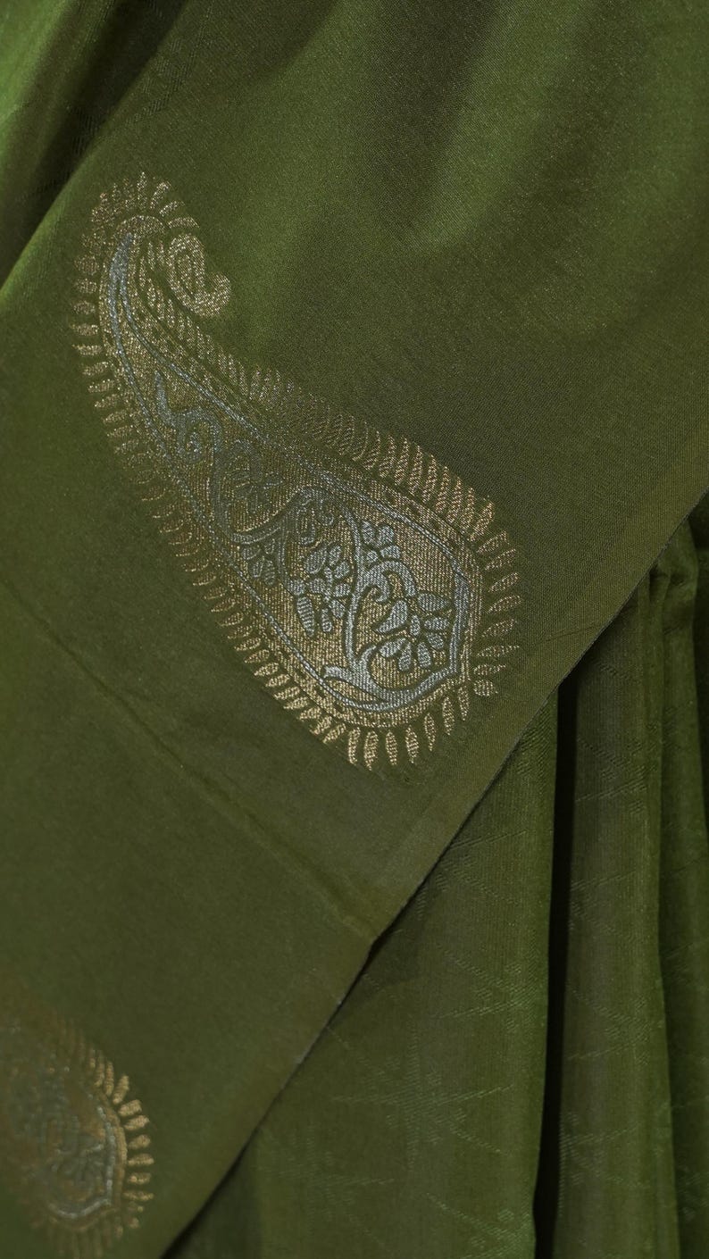 Puede incluir: Tela verde oliva con un detallado dise&ntilde;o de cachemira en oro y plata. La tela est&aacute; doblada, mostrando el intrincado dise&ntilde;o y la textura. La est&eacute;tica general es elegante y sofisticada.