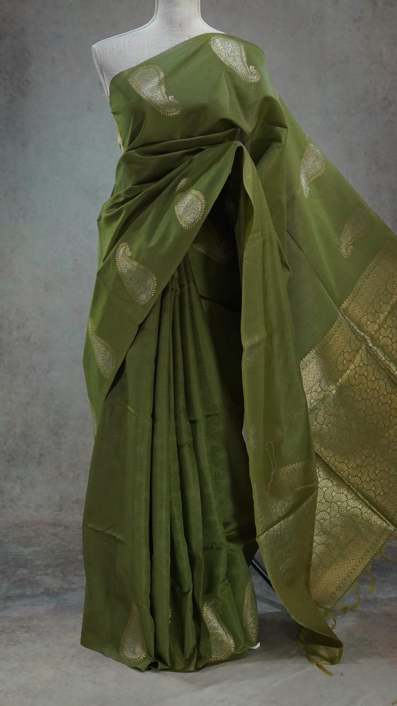 Puede incluir: Sari verde oliva con motivos de cachemira dorados y un borde dorado decorativo. La tela se drapea elegantemente, mostrando el intrincado dise&ntilde;o. Esta prenda tradicional es adecuada para ocasiones especiales.