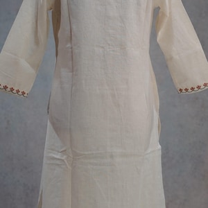 Puede incluir: Vestido t&uacute;nica color crema de manga larga. El vestido presenta un corte sencillo y relajado con cuello redondo y mangas largas. Los pu&ntilde;os est&aacute;n adornados con un patr&oacute;n bordado decorativo en color marr&oacute;n rojizo. La tela parece ligera.