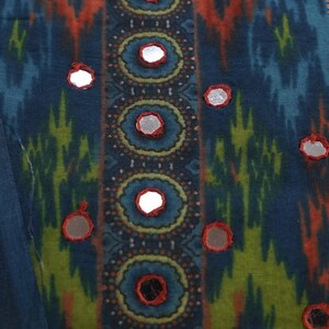 May include: Close-up of a textile with a vibrant, patterned design. The fabric features a mix of blue, orange, and green hues. Decorative mirrored accents are evenly spaced across the surface, adding a touch of sparkle to the overall aesthetic.