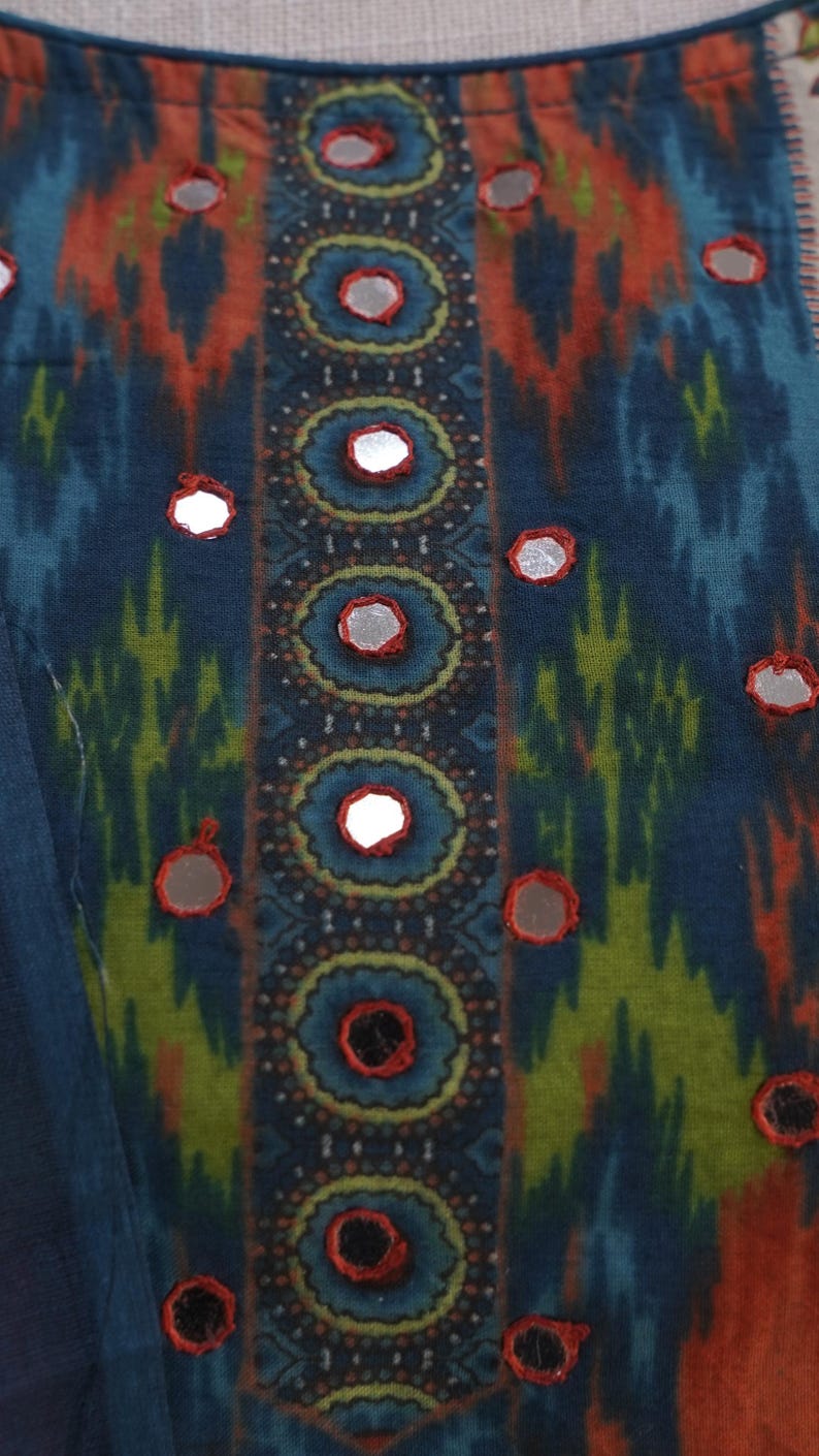 May include: Close-up of a textile with a vibrant, patterned design. The fabric features a mix of blue, orange, and green hues. Decorative mirrored accents are evenly spaced across the surface, adding a touch of sparkle to the overall aesthetic.
