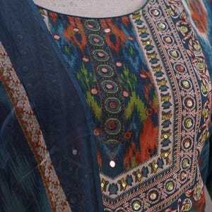 May include: A vibrant, patterned tunic and scarf set. The tunic features a round neckline with a detailed border of orange, green, and blue designs, embellished with small mirrors. The scarf has a matching border.