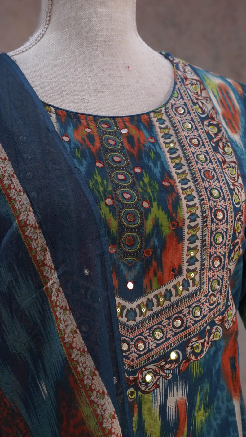 May include: A vibrant, patterned tunic and scarf set. The tunic features a round neckline with a detailed border of orange, green, and blue designs, embellished with small mirrors. The scarf has a matching border.