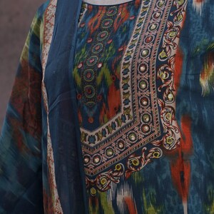 May include: A teal-colored tunic with a patterned design in orange, green, and white. The neckline and sleeves are adorned with intricate embellishments. The fabric appears to be lightweight and flowing, suitable for warm weather.