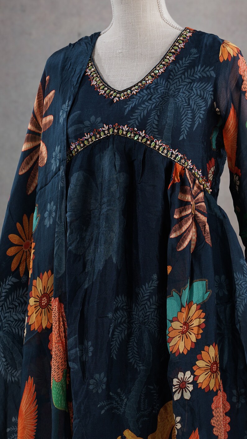 May include: A dark blue dress with a V-neckline, adorned with colorful floral and leaf patterns in orange, yellow, and green. The neckline is embellished with colorful beads. The dress is displayed on a mannequin.