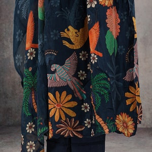 May include: Dark navy blue ensemble featuring a flowing top and matching pants. The fabric is adorned with a vibrant print of colorful parrots, flowers, and palm trees. The outfit is displayed on a white stand, showcasing the intricate design.