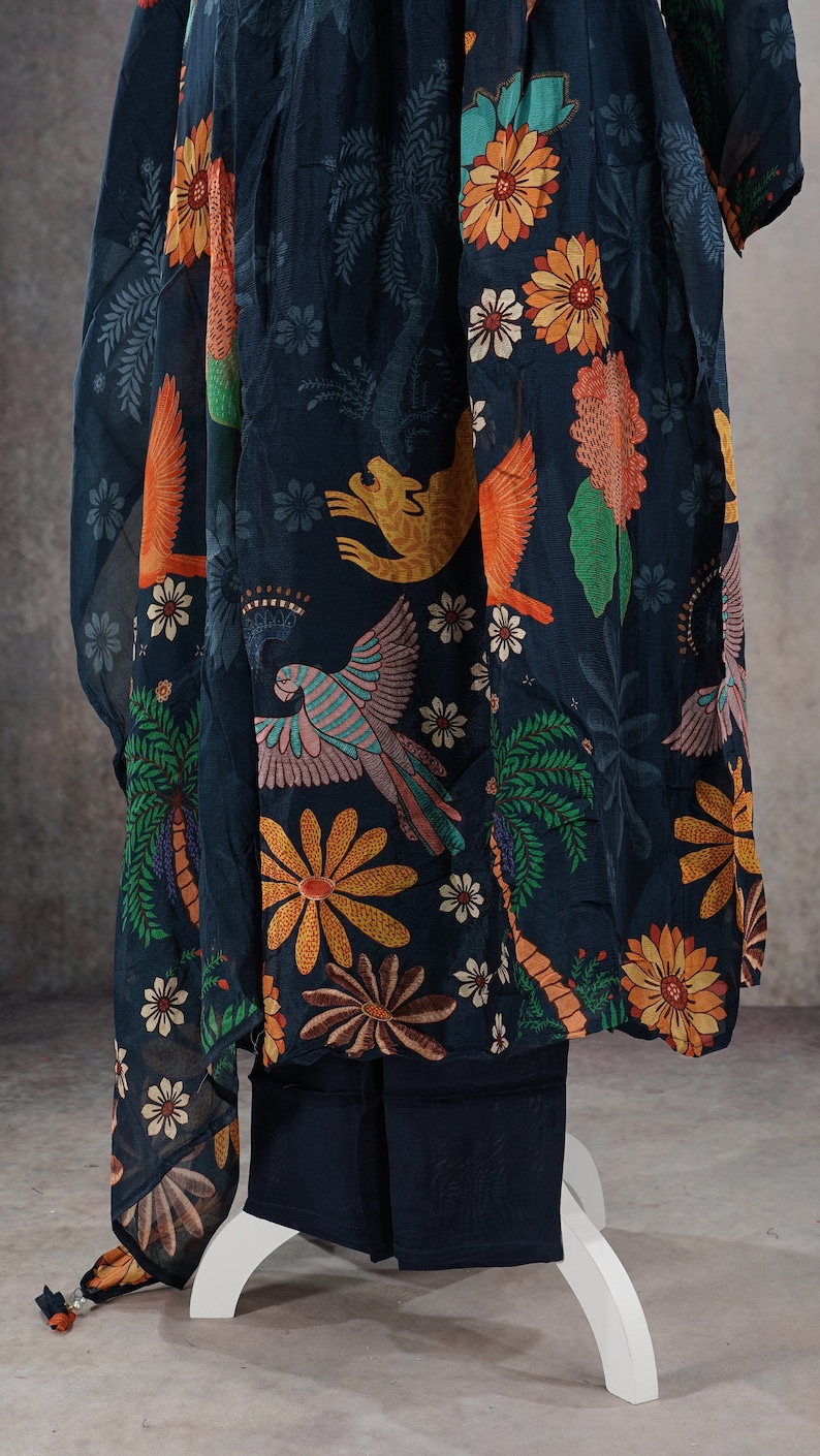 May include: Dark navy blue ensemble featuring a flowing top and matching pants. The fabric is adorned with a vibrant print of colorful parrots, flowers, and palm trees. The outfit is displayed on a white stand, showcasing the intricate design.