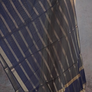 May include: A navy blue scarf with gold vertical stripes. The scarf has a gold border and is draped over a mannequin. The fabric appears lightweight and flowing, suitable for warmer weather.