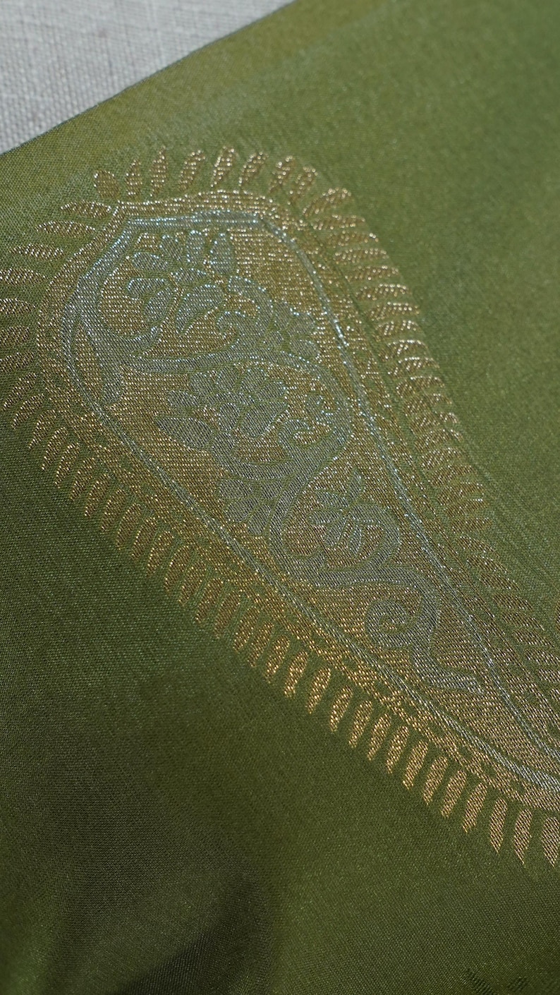 Puede incluir: Primer plano de un textil verde con un dise&ntilde;o de cachemira dorado y plateado. El intrincado patr&oacute;n est&aacute; detallado con elementos florales y curvos. La tela tiene un brillo sutil y el dise&ntilde;o est&aacute; centrado en el textil.