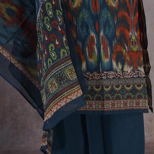 May include: A teal-colored ensemble featuring a patterned top and matching pants. The top has a vibrant ikat-style design in shades of teal, orange, and yellow. The pants are a solid teal color. The outfit includes a patterned scarf.