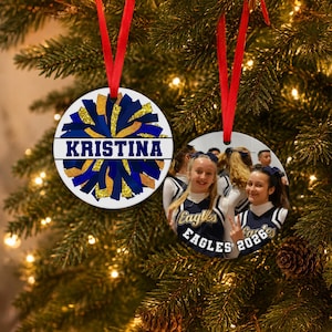 Personalized pom pom ornament showing a blue and gold custom cheerleader ornament 2026 hanging on a tree with a team photo.