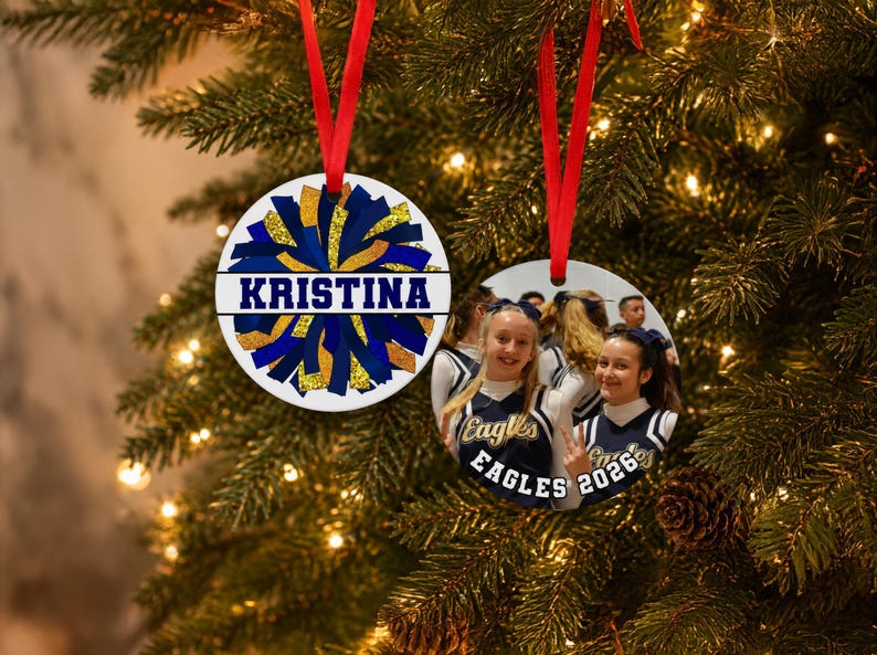 Personalized pom pom ornament showing a blue and gold custom cheerleader ornament 2026 hanging on a tree with a team photo.