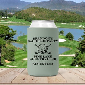 May include: A light sage green foam beverage can cooler featuring black text that reads BRANDON'S BACHELOR PARTY, PINE LAKE COUNTRY CLUB, AUGUST 2023, and a graphic of a golf ball centered between two crossed golf clubs.