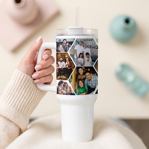 May include: White travel mug with a handle, featuring a collage of family photos in a geometric pattern. The mug has a clear lid and a white straw. The mug is held by a person wearing a cream-colored sweater.
