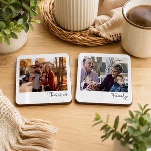 May include: Two square coasters with a white border resembling a polaroid frame. The left coaster features a family photo and the text "This is us". The right coaster displays a photo of three people and the text "Family". Both have a dark wood base.