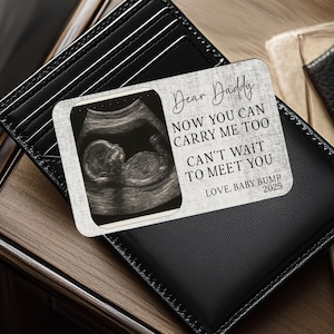 May include: A rectangular wallet insert card featuring a black and white ultrasound image of a fetus on the left side. The right side displays the text: Dear Daddy, NOW YOU CAN CARRY ME TOO, CAN'T WAIT TO MEET YOU, LOVE, BABY BUMP 2025.