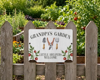 May include: A rectangular garden sign with a white wood-grain background features the text "GRANDPA'S GARDEN" at the top and "LITTLE HELPERS WELCOME" at the bottom. Illustrations of a trowel, pruning shears, and a hand fork sit between two tomato plants.
