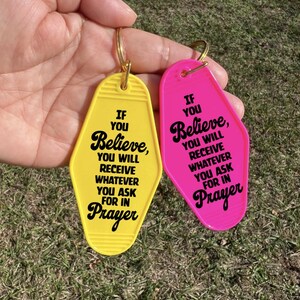 May include: Two motel-style keychains, one yellow and one pink, with gold key rings. The yellow keychain has the text "If You Believe, You Will Receive Whatever You Ask For In Prayer" in black. The pink keychain has the same text.