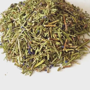 Puede incluir: Un montón de hierbas secas, con tonos verdes, marrones y morados. Las hierbas parecen ser una mezcla de tallos, hojas y pequeñas flores. La imagen está tomada desde arriba, con las hierbas sobre una superficie blanca.