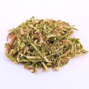 Può includere: Primo piano di un mucchio di erbe essiccate, prevalentemente verdi con steli e foglie marroni e rossastre. Le erbe sono disposte su una superficie bianca, evidenziando la consistenza e i dettagli del materiale vegetale.