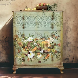 May include: A vintage dresser with five drawers painted in a light green color. The drawers are decorated with a floral design and a lace pattern. The dresser is sitting on a wooden floor with a brown background.