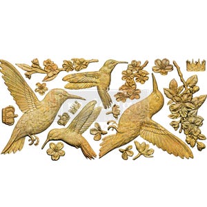 May include: Gold-colored hummingbird and floral embellishments. The design features three hummingbirds in various poses, along with flowers, leaves, and small crowns. The elements are detailed and appear to be made of metal.