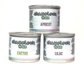 May include: Three stacked metal tins of Chameleon Wax. The top tin is labeled "Apricot", the bottom left tin is labeled "Cactus", and the bottom right tin is labeled "Lilac". Each tin has a silver lid and a colorful, iridescent band around the base.