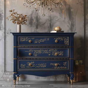 May include: A navy blue dresser with three drawers, each decorated with gold script writing. The dresser has gold accents on the drawer pulls and along the top and bottom edges of the drawers. The dresser is sitting on a wooden floor.