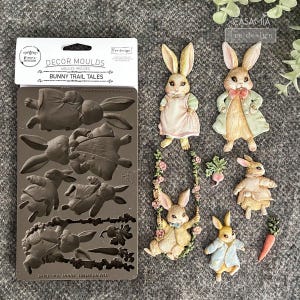 May include: A collection of bunny-themed craft supplies. Includes a silicone mold with bunny designs and several painted bunny figurines with accessories like a swing, carrot, and radish. The mold is dark brown, and the bunnies are pastel-colored.