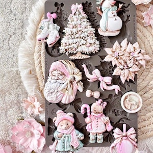 May include: A dark gray silicone mold featuring various Christmas-themed shapes including a Santa Claus, a snowman, a decorated tree, a gingerbread person, a bear, ice skates, a poinsettia, a bow, and a round ornament with a deer design.