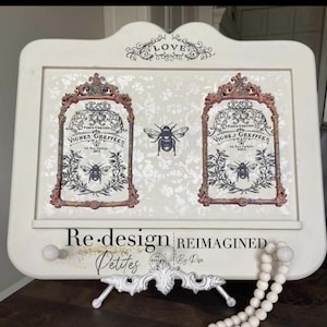 May include: A white decorative wall hanging with two framed bee and floral designs. The frames are accented with red and gold trim. The words "LOVE" and "Re-design Reimagined Petites" are also visible.