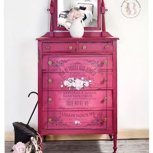 May include: A vibrant fuchsia dresser featuring two small top drawers and four large lower drawers with gold-toned knobs. The front displays black French text and floral illustrations. A mirror is attached to the top with a white pitcher.