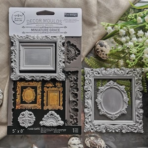 May include: A gray silicone mold set for crafting, featuring ornate frame designs and decorative elements. The package includes a variety of shapes, including rectangular and oval frames, with dimensions of 5 inches by 8 inches. The mold is food safe.