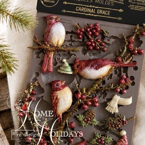 May include: A gray silicone decor mould titled Cardinal Grace featuring raised designs of red cardinals perched on branches with berries, pinecones, a small hat, and a scarf. The top header includes the text Decor Moulds and Cardinal Grace.