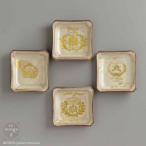 May include: Four square decorative plates with a cream-colored background and gold accents. Each plate features a different design with text, including "Paris" and "Green's Nursery". The plates have a distressed, vintage look with brown edges.